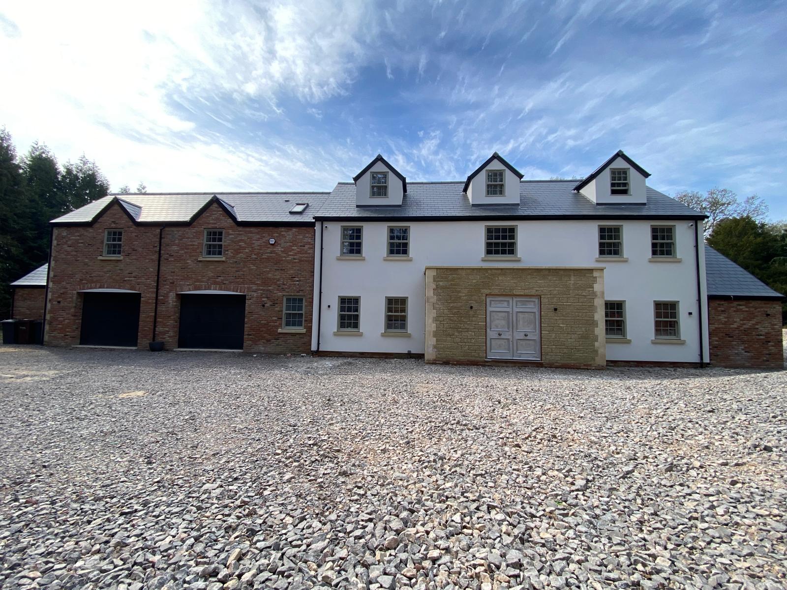 Two-storey luxury home with white render, red brick wing, stone porch and gravel driveway