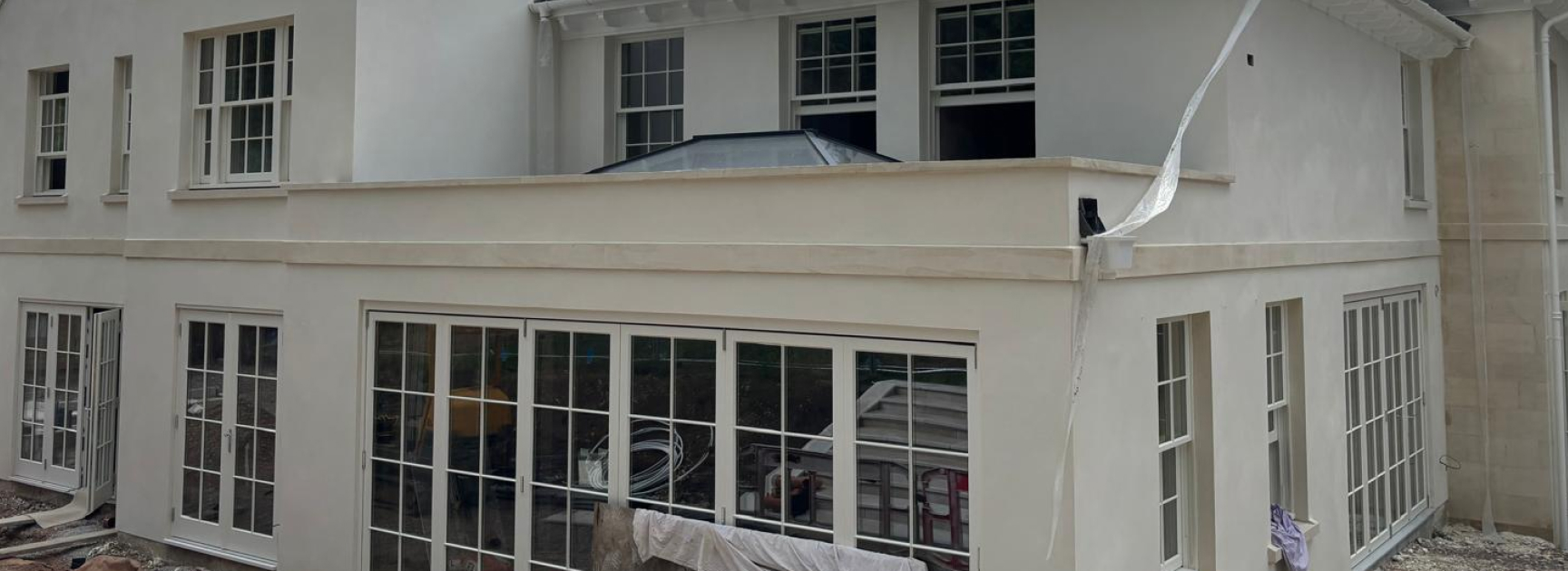 Wide view of a cream rendered two-storey house with sash windows and large bifold doors