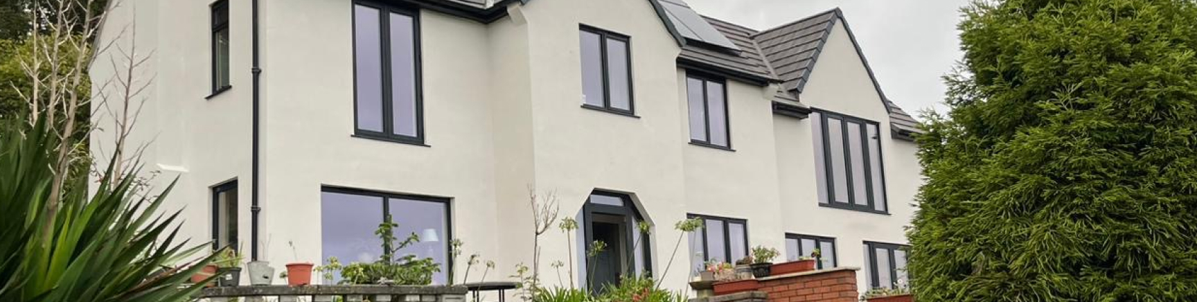 Modern two-storey white rendered house with dark window frames, solar panels and landscaped terrace