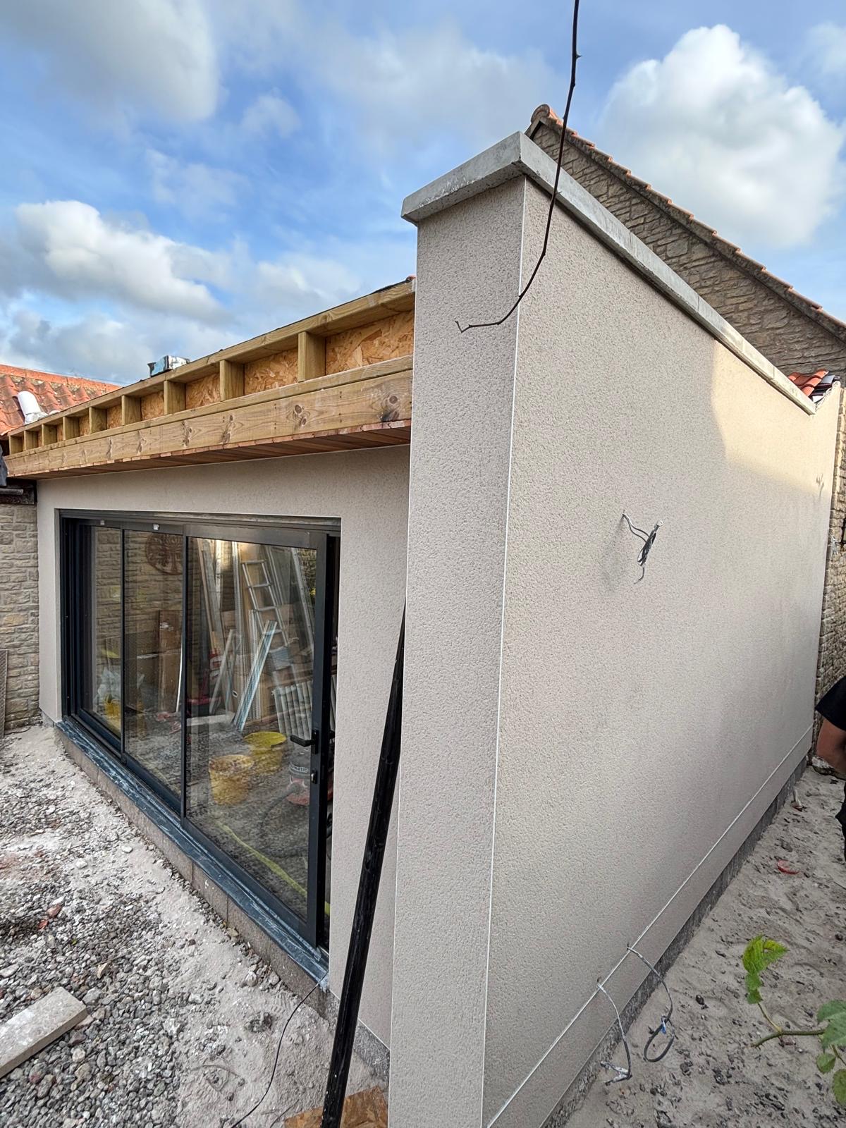 Cream rendered flat-roof extension with black sliding doors under construction