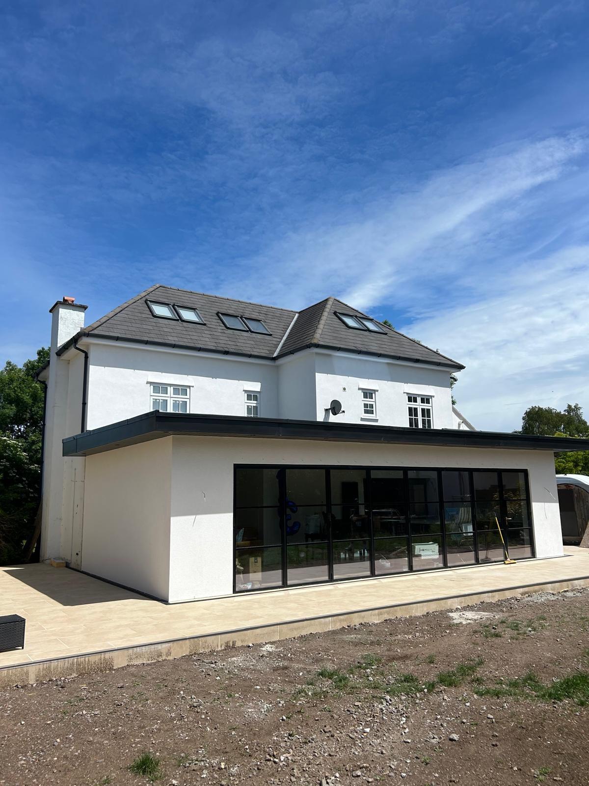 White rendered two-storey house with black bifold doors, skylights and new patio