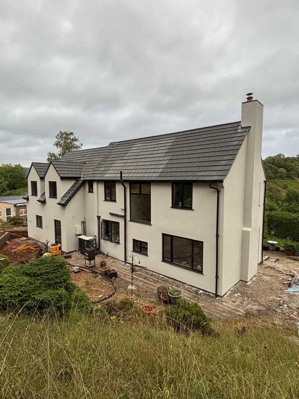 Two-storey cream rendered house with black window frames on a hillside garden plot